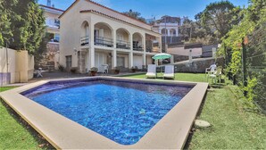 A rectangular swimming pool with a tiled edge, surrounded by a grassy area and a building with a tiled roof and arched balconies. - House in Roses With Pool Near La Punta Beach (Roses)
