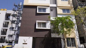 A multi-story residential building with a gated entrance, a parked motorcycle, and construction scaffolding on the right side. - VISTA LIVING (Kasavanahalli)