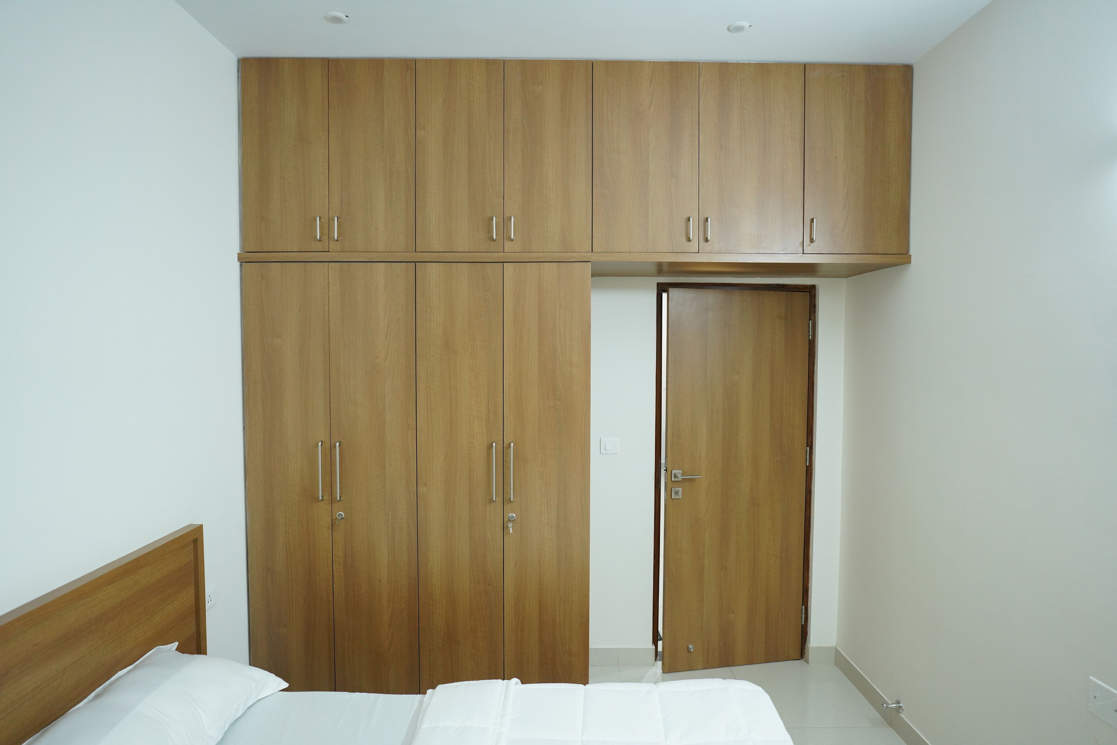 A bedroom with a wooden wardrobe, a bed, and a door.