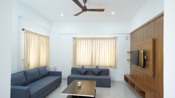 A modern living room with a sofa, a coffee table, and a TV mounted on a wooden panel. - VISTA LIVING (Kasavanahalli)