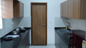 A compact kitchen with wooden cabinets, a black countertop, a stainless steel sink, and a door with a handle. - VISTA LIVING (Kasavanahalli)