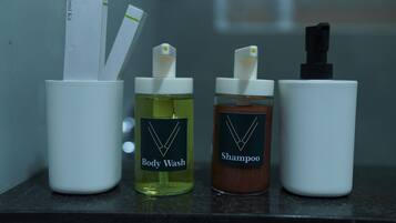 Four white containers on a countertop, each labeled with a different product: Body Wash, Shampoo, and two others with labels not visible.