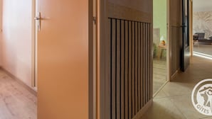 Un pasillo con suelo de madera, pared color beige y puerta con manija metálica.