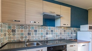 Una cocina con azulejos decorativos en la pared, armarios de madera, un lavamanos de acero inoxidable y un microondas.
