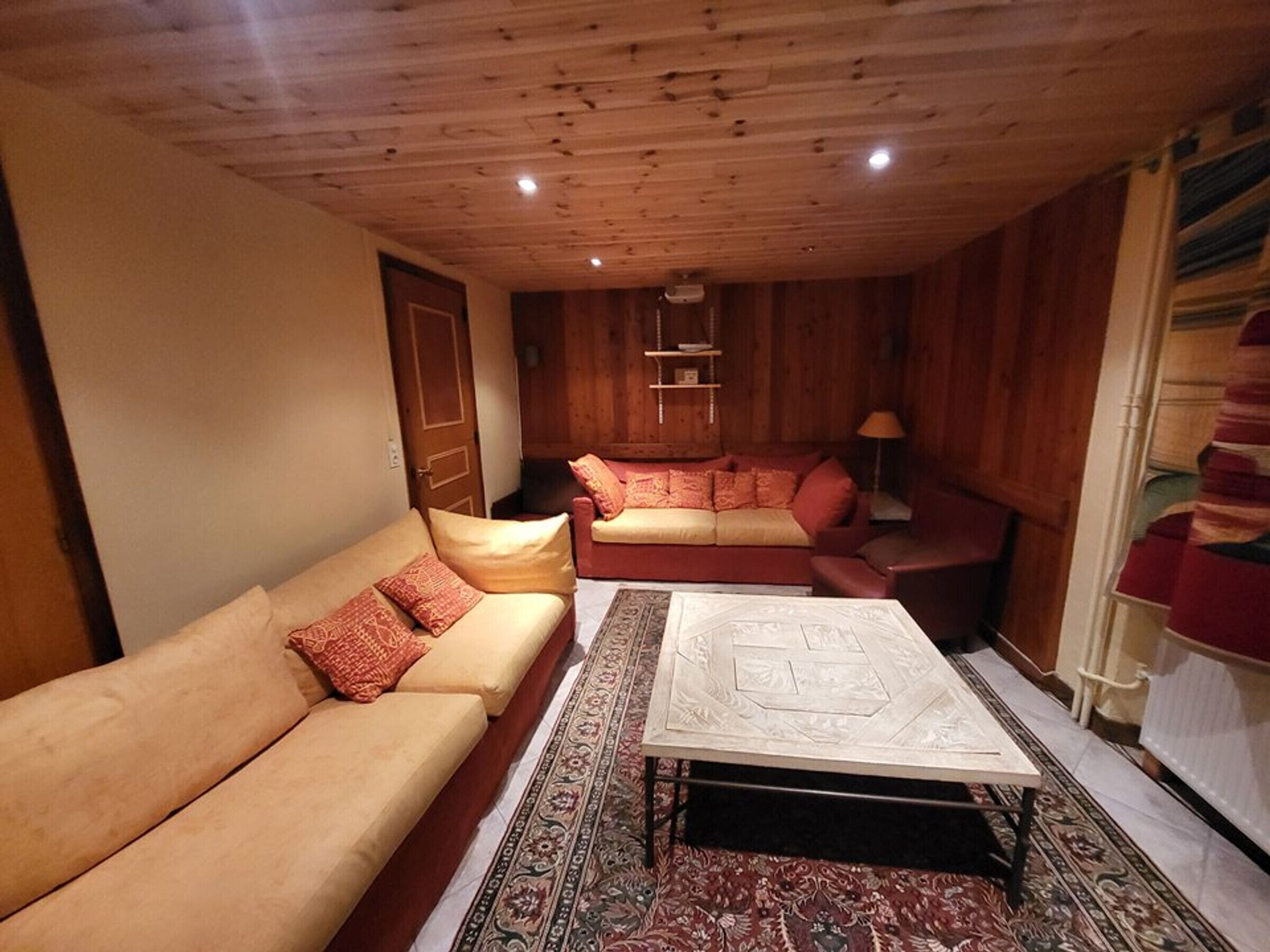 A cozy living room with a beige sofa, a red sofa, and a patterned rug.