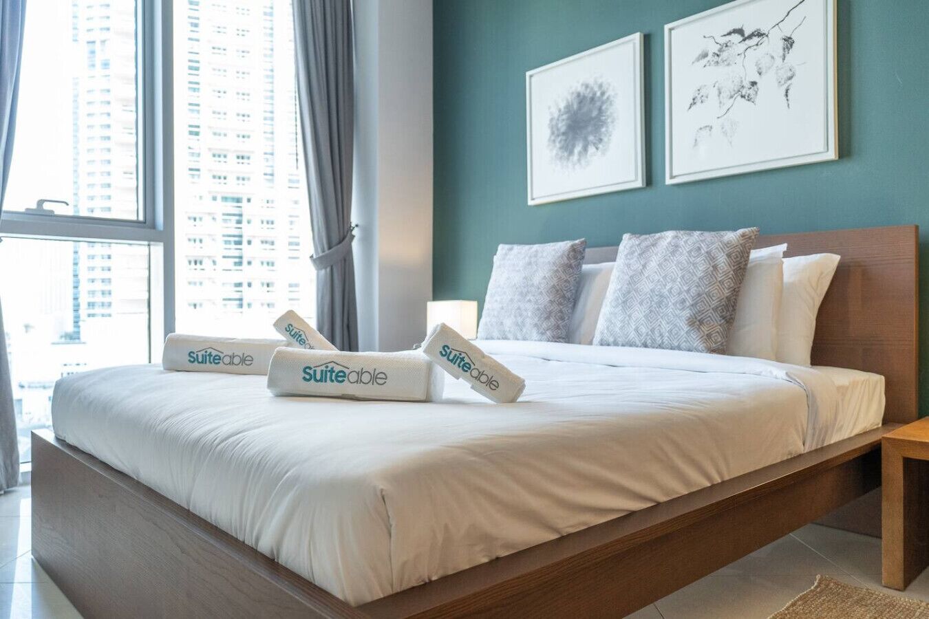Una habitación de hotel con una cama grande, cabecera de madera, dos cuadros enmarcados en la pared y una ventana con cortinas.