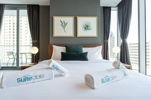 A hotel room with a large bed, two pillows, two framed botanical prints on the wall, and a view of the city through the window. - Premium 2 Bedroom in Trident Residence JBR (Dubai)