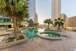 Um hotel moderno com piscina central, palmeiras e arranha-céus ao fundo.