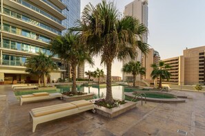 Un patio moderno de hotel con piscina, palmeras y zonas de estar.