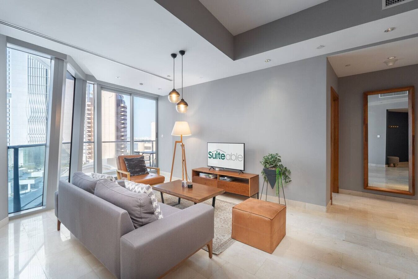 A modern living room with a grey sofa, wooden coffee table, and a television displaying 'Suiteable'.