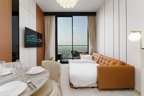 Habitación de hotel con cama, sofá, mesa de comedor con platos y vasos, televisor y un ventanal con vistas.