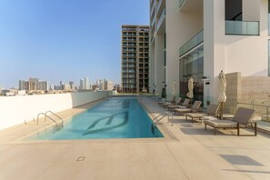 Una piscina en la azotea con sillones de descanso y vista al horizonte de la ciudad.