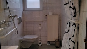 Une salle de bain avec des toilettes, un lavabo, une douche et un carrelage à motifs carrés.