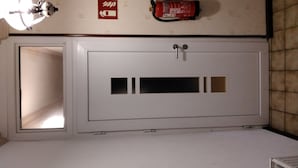 Un placard blanc avec une petite fenêtre, un extincteur et un luminaire fixé au mur.