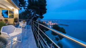 Un balcón con mobiliario exterior, con vistas a un paisaje urbano costero al atardecer.