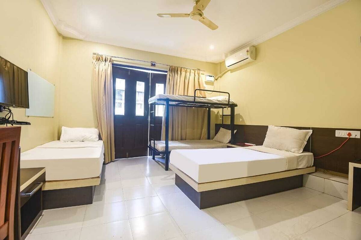 Quarto de hotel com duas camas de solteiro, uma cama beliche, uma escrivaninha com cadeira, televisão e aparelho de ar condicionado.
