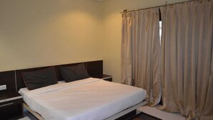 A bedroom with a single bed, a nightstand, and beige curtains. - Vihasta Sunrise Hotel by RR Enterprises (Margao)