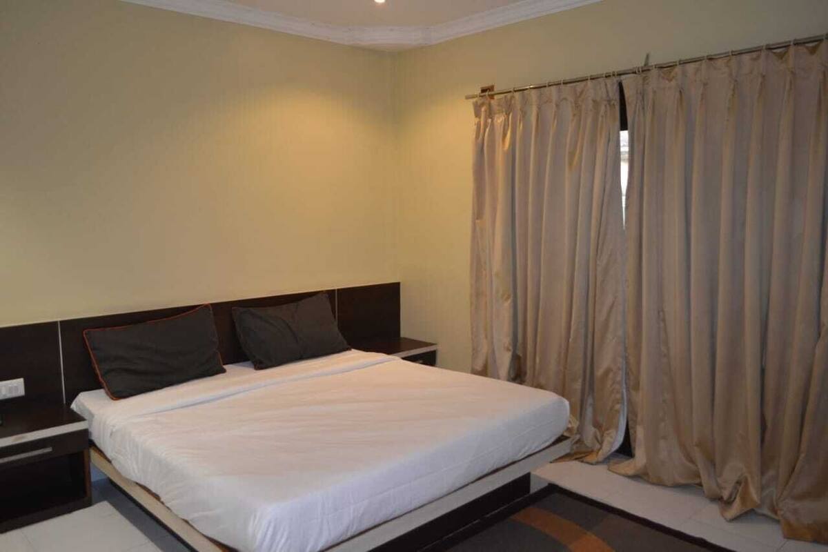 Quarto com uma cama de solteiro, mesa de cabeceira e cortinas bege.