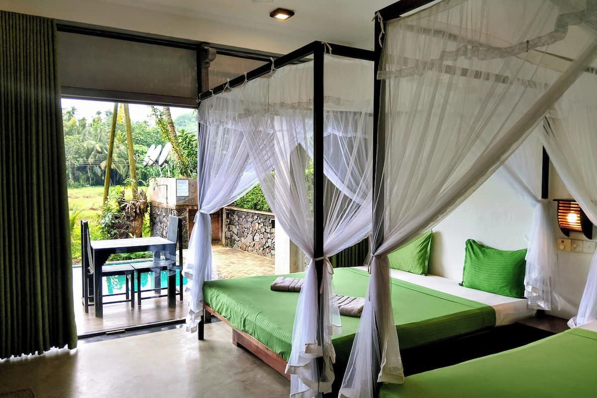 A room with a bed, green bedding, a table, and a chair.