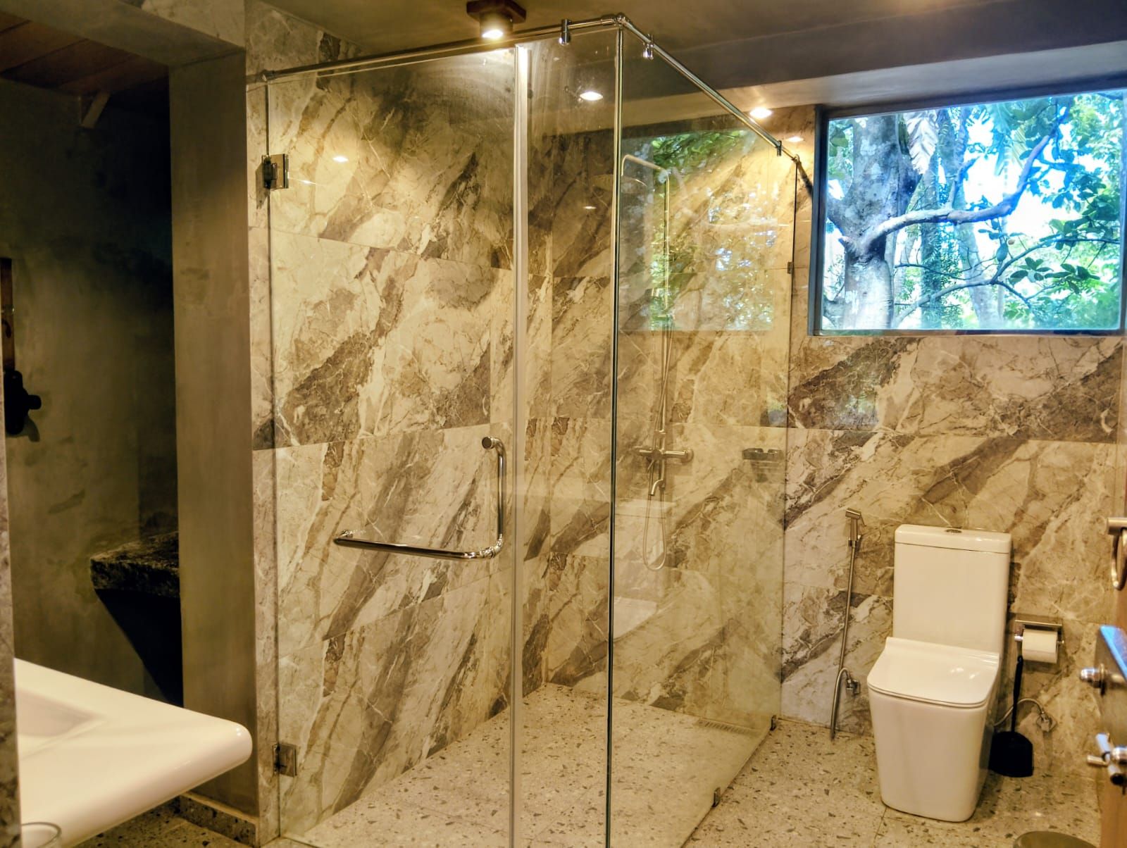 Une salle de bain moderne avec une douche à parois de verre, des murs en marbre, des toilettes et un lavabo.