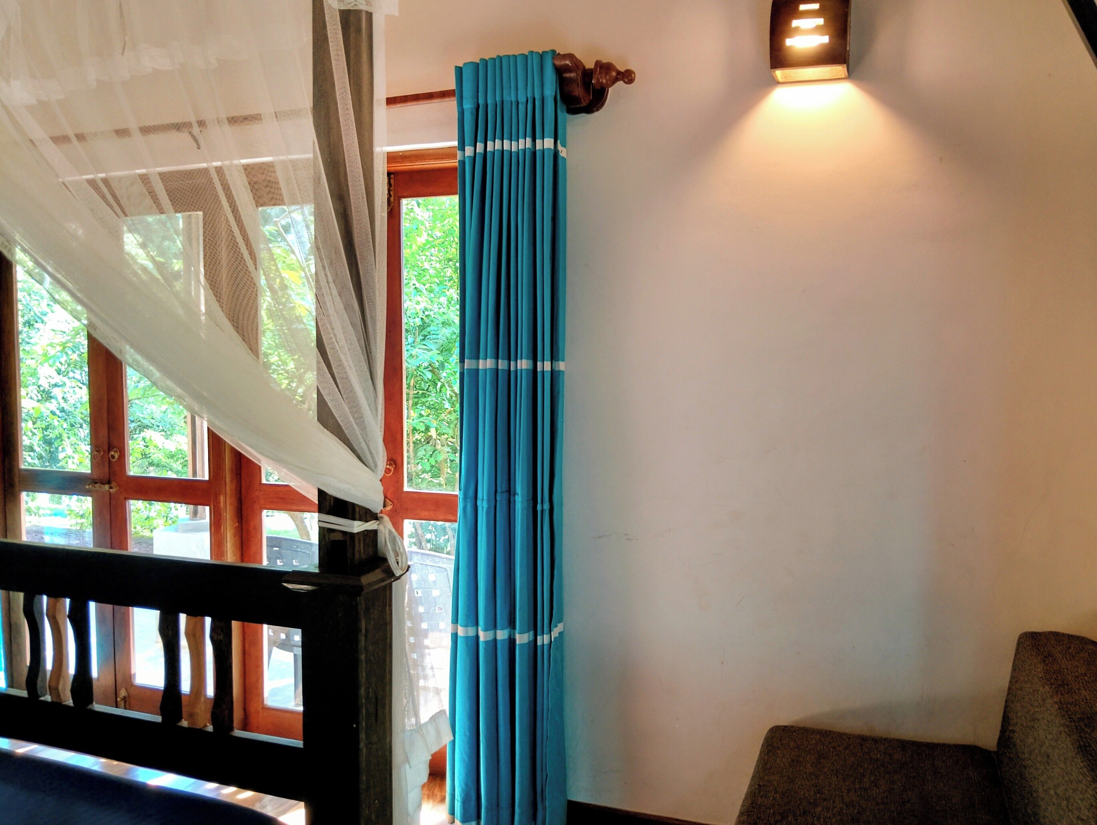 A room with a window, a curtain, a wall-mounted light, and a wooden railing.