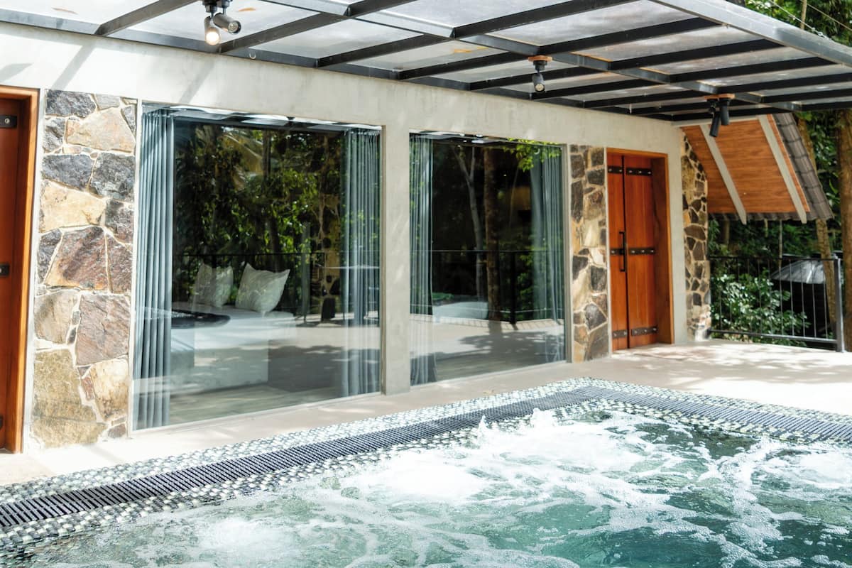 A modern house with a glass-enclosed patio, a hot tub, and a stone exterior.