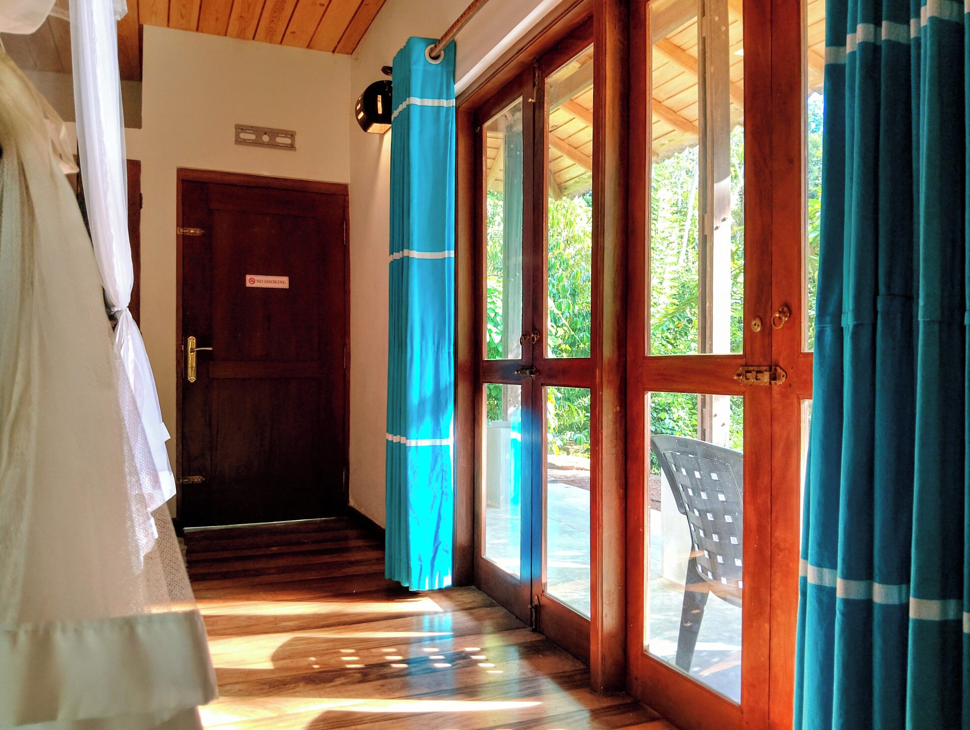 A wooden door with a 'No Smoking' sign, a blue curtain, and a view of greenery outside.