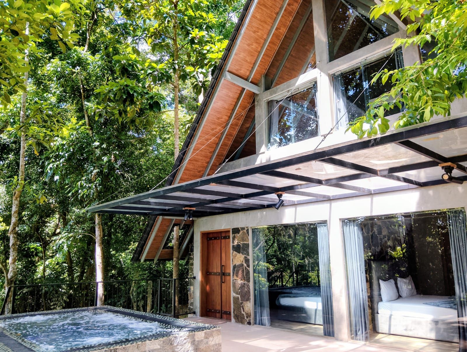 Une maison moderne dotée d’un patio entièrement vitré, d’un jacuzzi et d’un lit visible à travers la vitre.