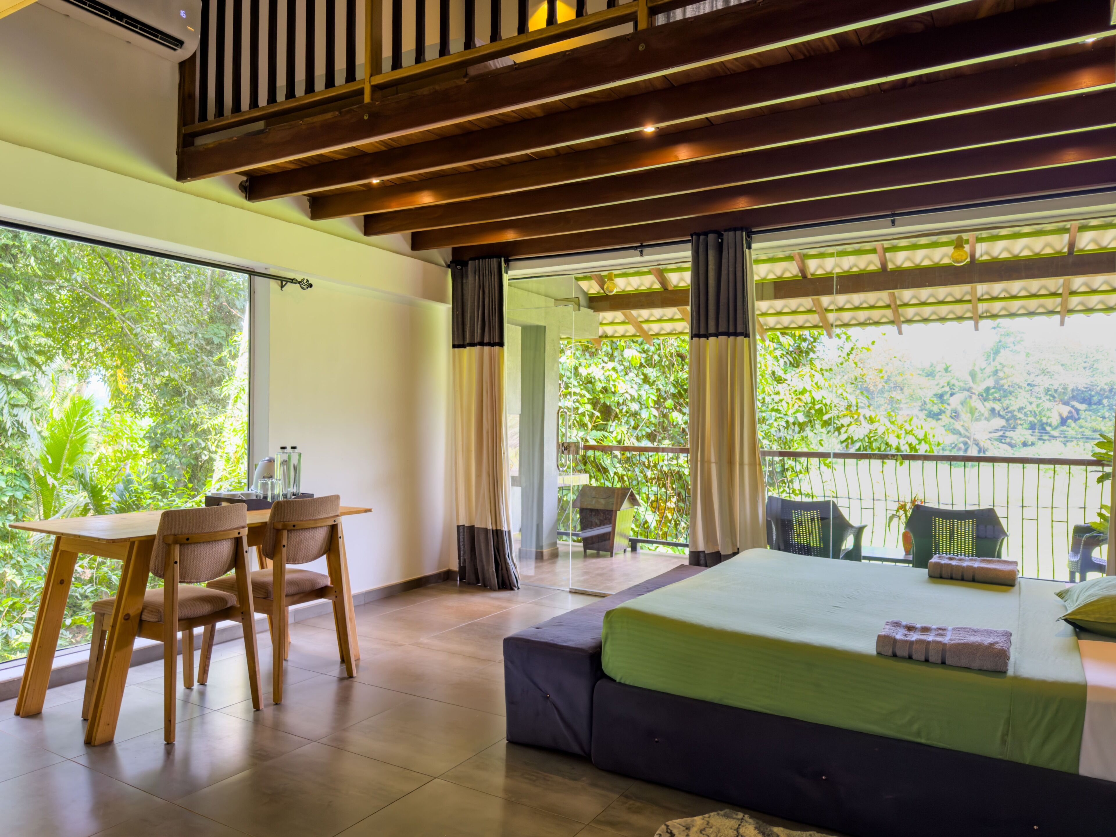 Una habitación con cama, escritorio, sillas y un balcón con vistas a zonas verdes.