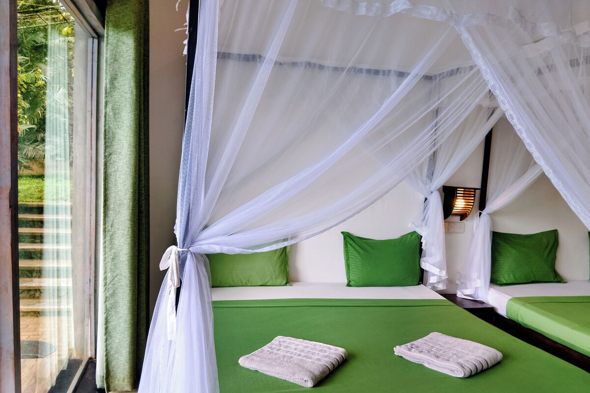 Een kamer met een bed, groene kussens, een witte hemel en een nachtlampje.
