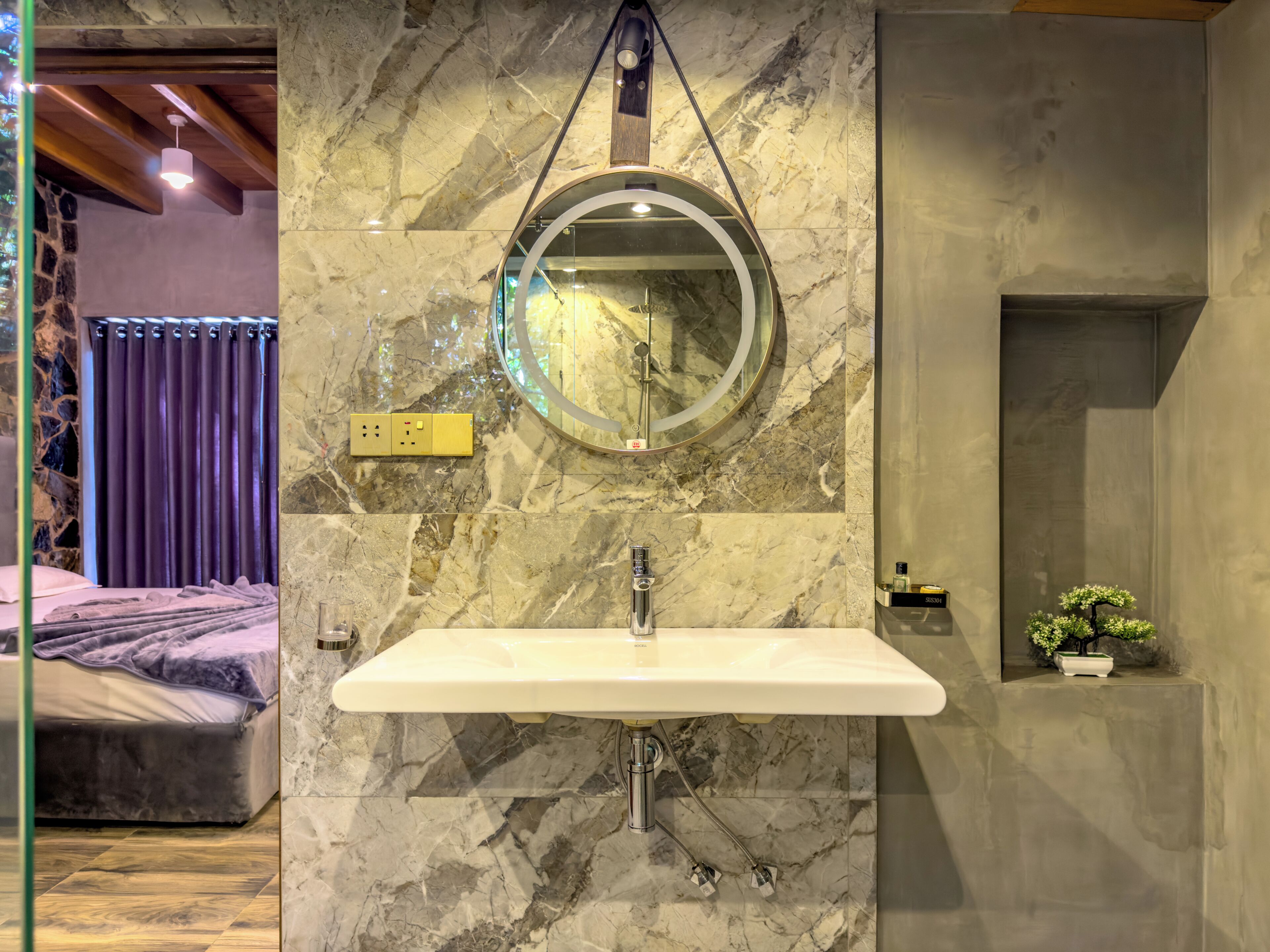 A bathroom with a marble sink, a round mirror, and a small potted plant.