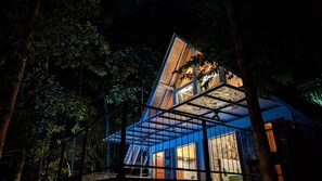 A modern, multi-level structure with a glass facade, surrounded by dense foliage. - Leisure Land Villas (SP)