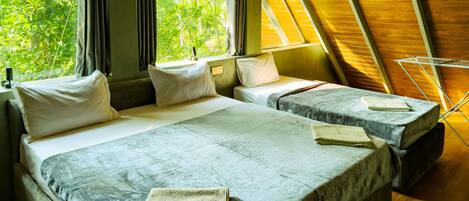 A room with two beds, a window with curtains, a wooden ceiling, and a view of greenery outside.