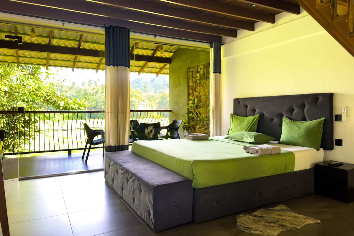 A bedroom with a bed, a bench, a nightstand, and a view of greenery.