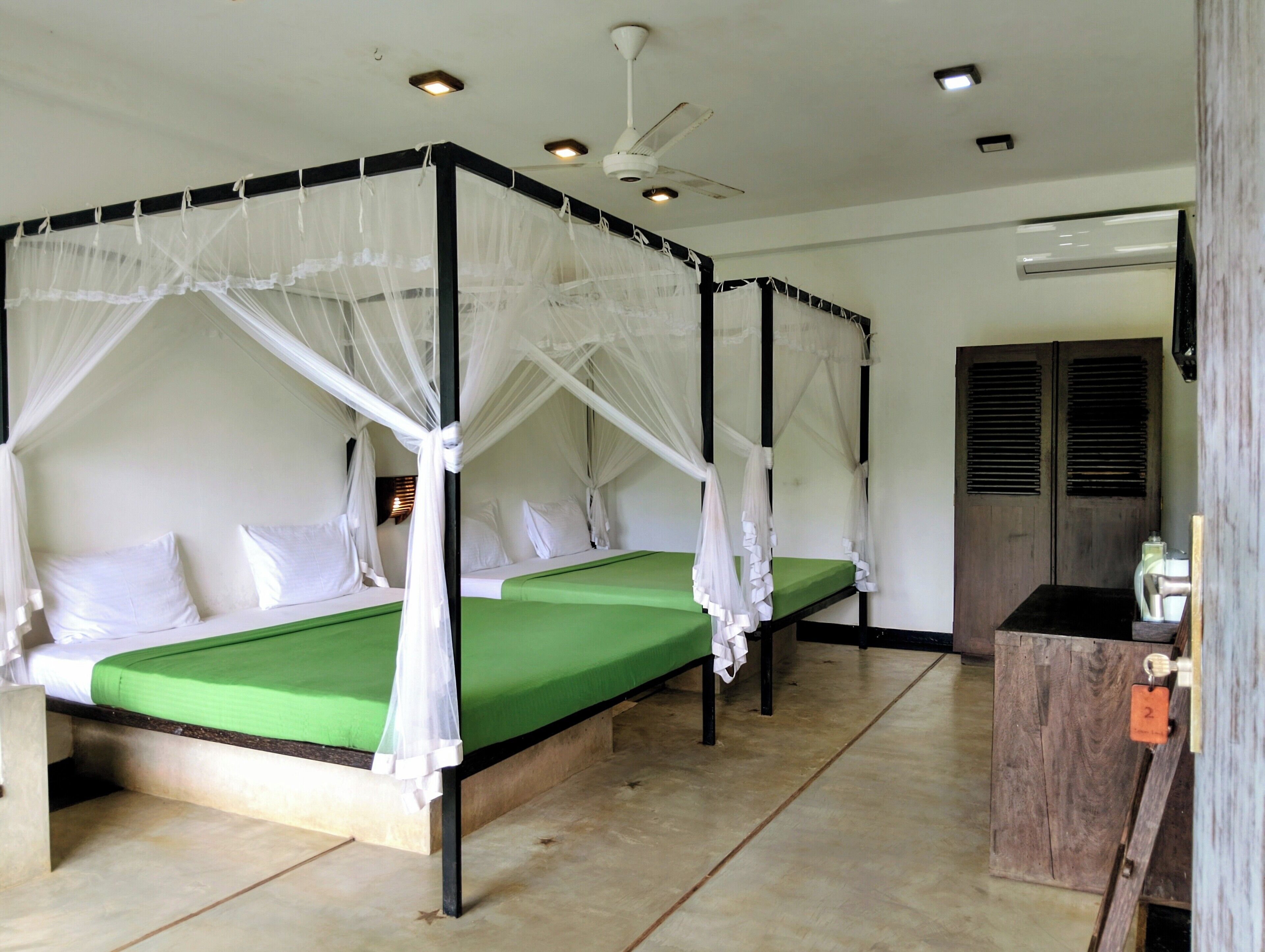 Een kamer met vier bedden, een hemelbed, een plafondventilator en een houten garderobe.