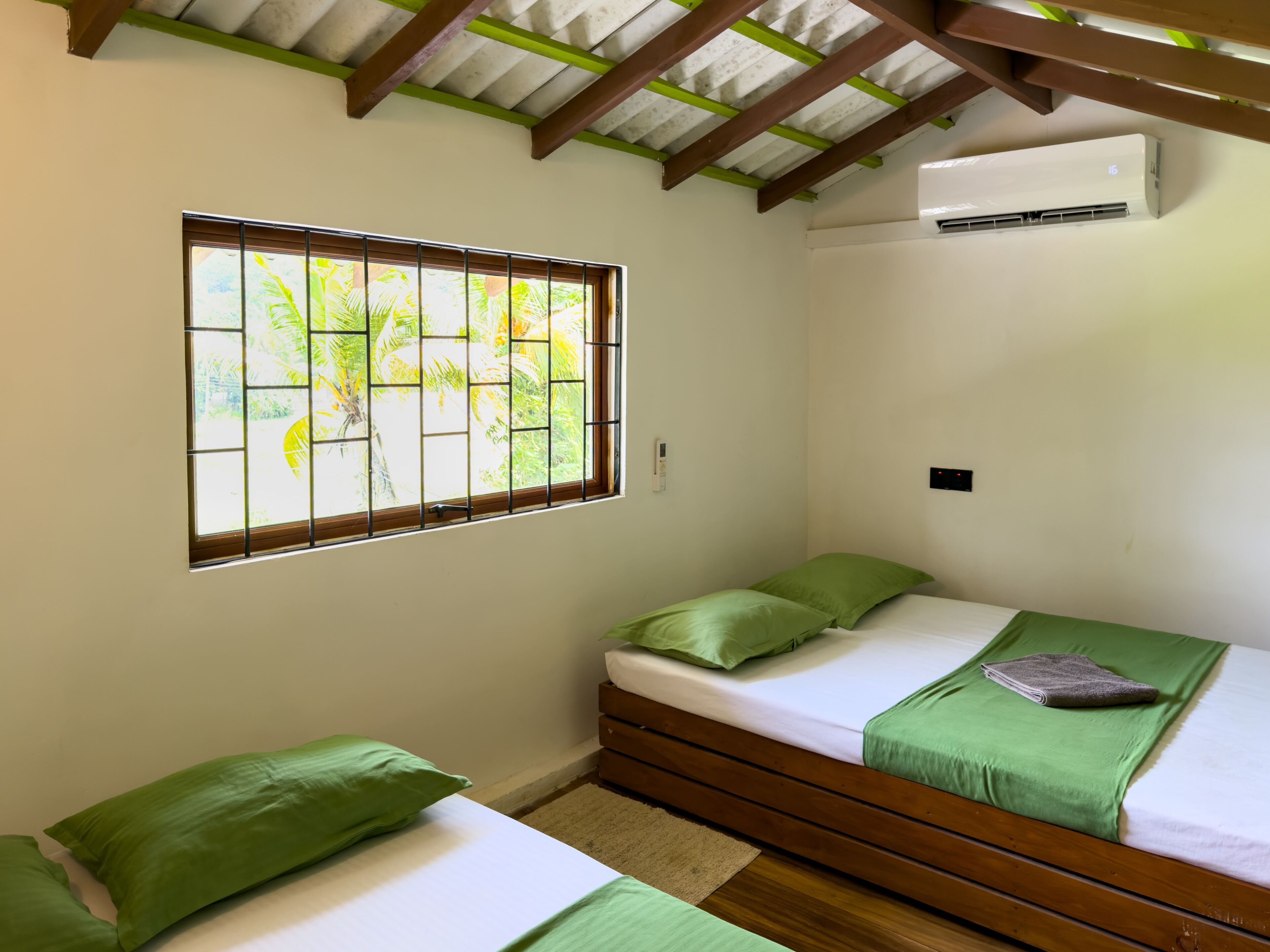 A bedroom with a window, a bed, a bedside table, and an air conditioning unit.