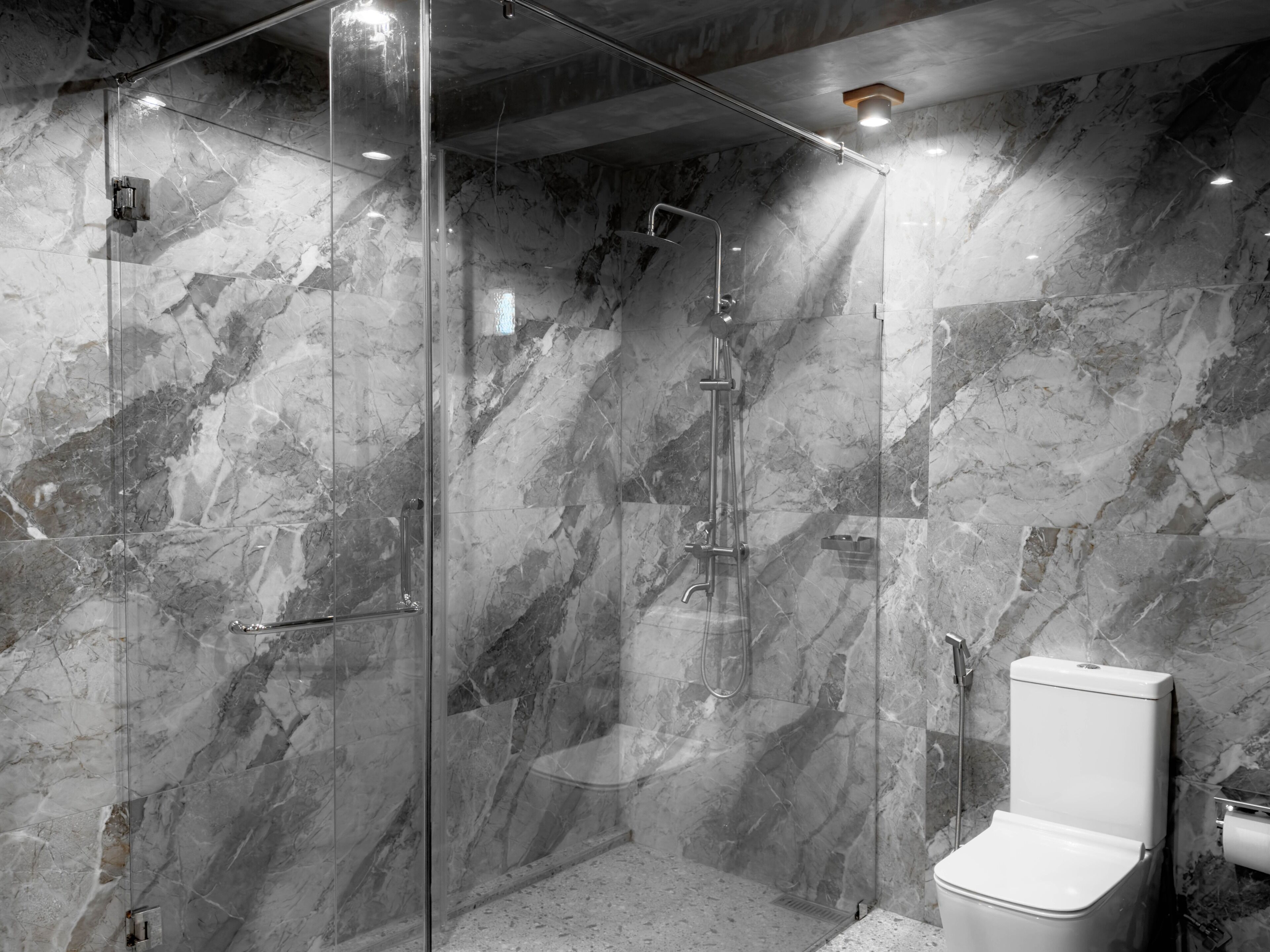 Ein modernes Badezimmer mit einer gläsernen Dusche, Marmorwänden und einer weißen Toilette.