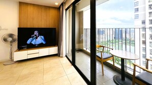 A modern living room with a flat-screen TV, a wooden accent wall, a balcony with a table and chairs, and a city view.