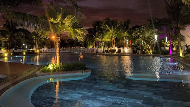 A nighttime pool area with palm trees and a white fence.