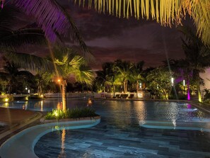 A nighttime pool area with palm trees and a white fence. - Sunny Vinhomes D'capitale (Hanoi)