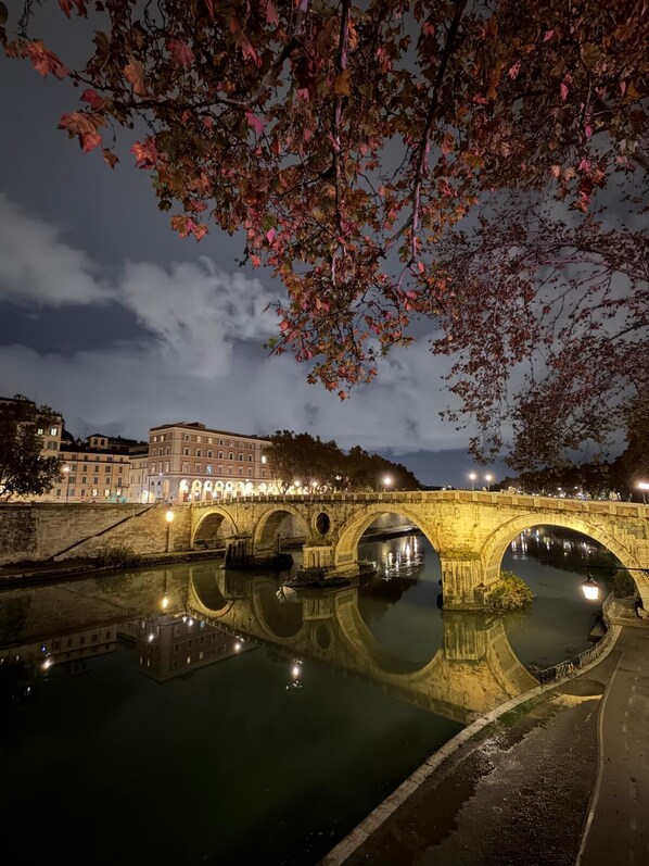 A stone bridge over a calm river at night, reflecting the bridge and surrounding buildings. - DOMUS COLOSSEUM, a few steps from the Colosseum (Roma)