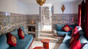 Un salon avec un canapé bleu, des coussins rouges, un mur à motifs et une petite table en bois.