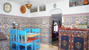 Une pièce avec un mur recouvert de carreaux, une table à manger avec des chaises bleues et un buffet orné de motifs décoratifs.