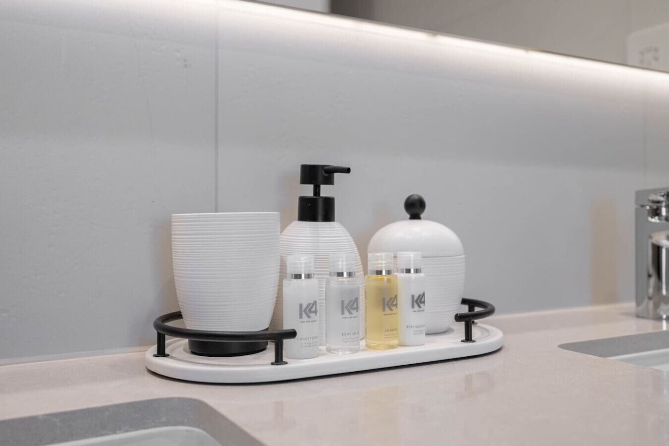 A bathroom vanity with a white sink, a black soap dispenser, and a tray holding various toiletries including a white bottle, a clear bottle, and a yellow bottle.