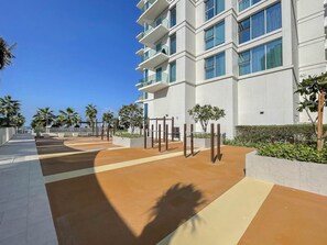 A modern building with multiple floors, large windows, and a paved walkway with palm trees and planters.
