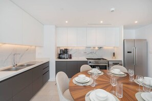 A modern kitchen with white cabinets, a stainless steel refrigerator, and a dining area set for four with a wooden table and white plates.