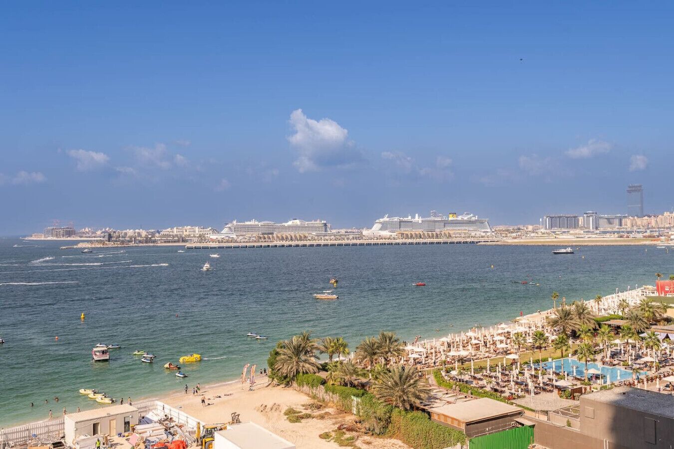 A coastal cityscape with a beach, cruise ships, and a marina.