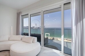 Ein modernes Wohnzimmer mit einer großen Eckcouch, einer Glasschiebetür, die auf einen Balkon mit Blick auf das Meer und ein Riesenrad führt.