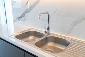 A modern kitchen with a double stainless steel sink, a sleek faucet, and a marble backsplash.