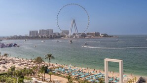 A beach with a large Ferris wheel in the background, a marina with boats, and a sandy area with umbrellas. - Beautiful 2 Bedroom Sea Views at La Vie JBR (Dubai)